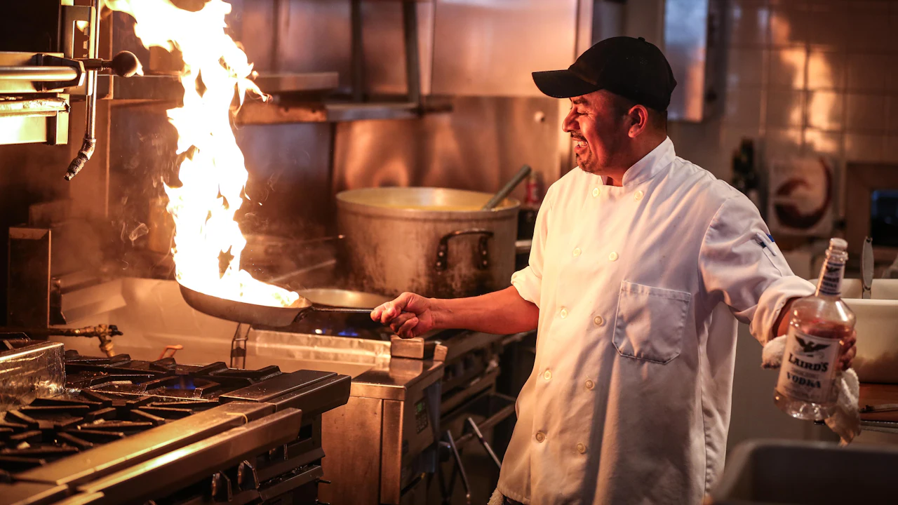 Chef flambéing a pan in a professional kitchen.